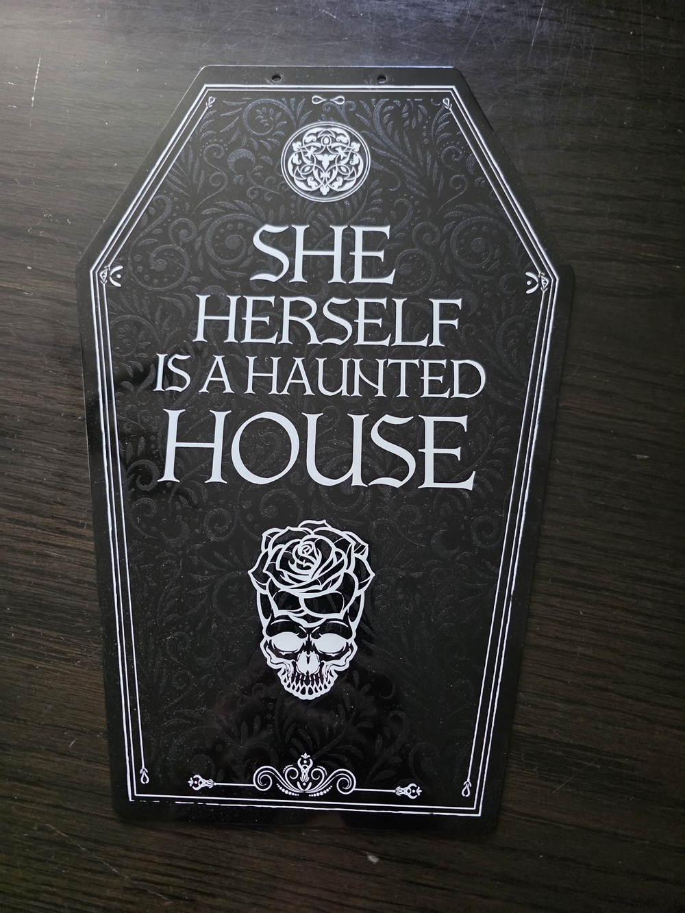 Coffin-shaped wall sign with bold white text reading "She Herself Is A Haunted H